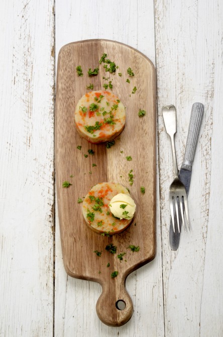 mashed potatoes with carrots, butter and parsley on a wooden board