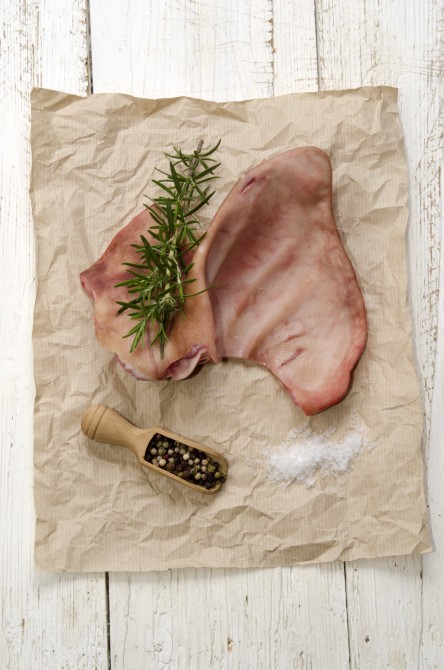 raw pig ear with rosemary, coarse salt and pepper on brown kitchen paper
