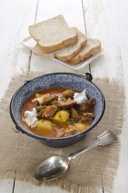 authentic hungarian goulash in a kettle with bell pepper, potato, carrot, sour cream and bread on a plate