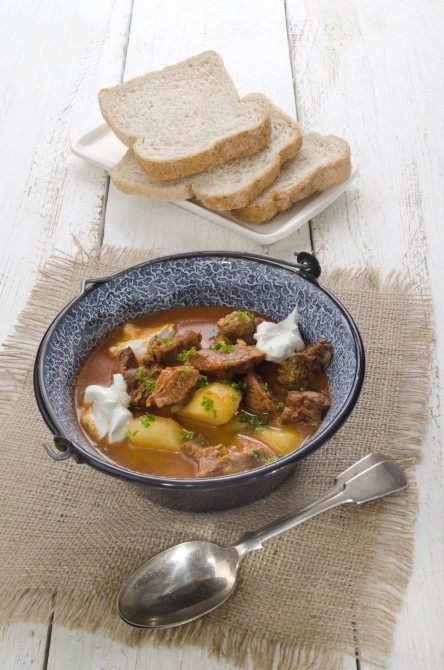 authentic hungarian goulash in a kettle with bell pepper, potato, carrot, sour cream and bread on a plate authentic hungarian goulash in a kettle with bell pepper, potato, carrot, sour cream and bread on a plate