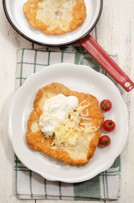 hungarian langos with sour cream, cheese and cherry tomato on a plate hungarian langos with sour cream, cheese and cherry tomato on a plate