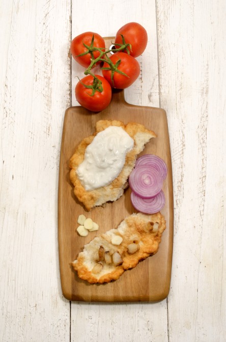 home made hungarian langos with lilac onion, grilled fat bacon, sour cream and tomato on a wooden board