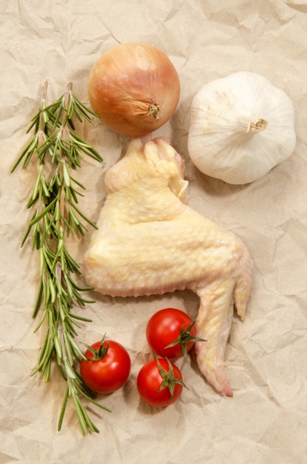 raw chicken wing with onion, garlic, cherry tomato and rosemary on brown kitchen paper 