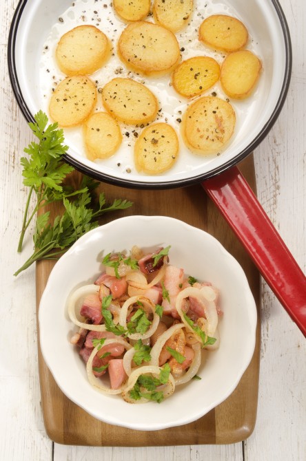 fried bacon and onion ring in a bowl, pan with sliced potato and parsley