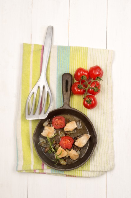 fried chicken fillet cubes with onion rings, tomato and rosemary in a cast iron pan fried chicken fillet cubes with onion rings, tomato and rosemary in a cast iron pan