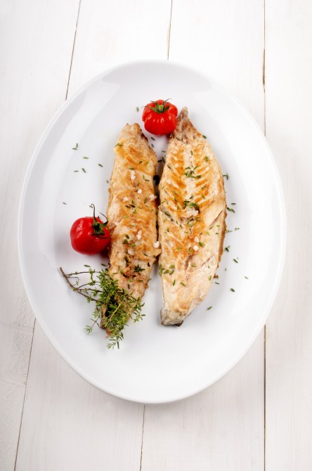 grilled mackerel with thyme and tomato on a white plate
