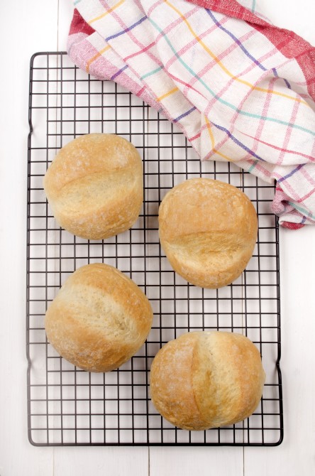 four bread rolls on a cooling rack with kitchen towel