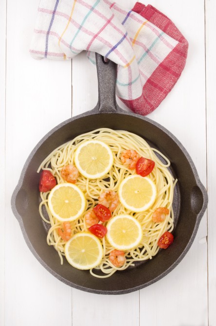 spaghetti with grilled prawns, tomato and lemon slice in a cast iron pan