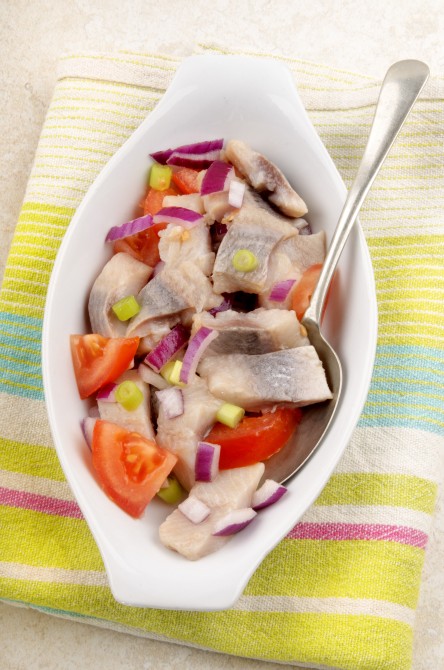 home made herring salad with tomato, purple onion and spring onions in a white bowl