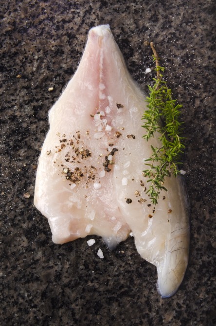 sea bream fillet with spice mix, coarse salt and thyme on a dark marble surface