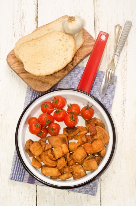 crackling with cherry tomato in a red enamel pan and slice bread on wooden board