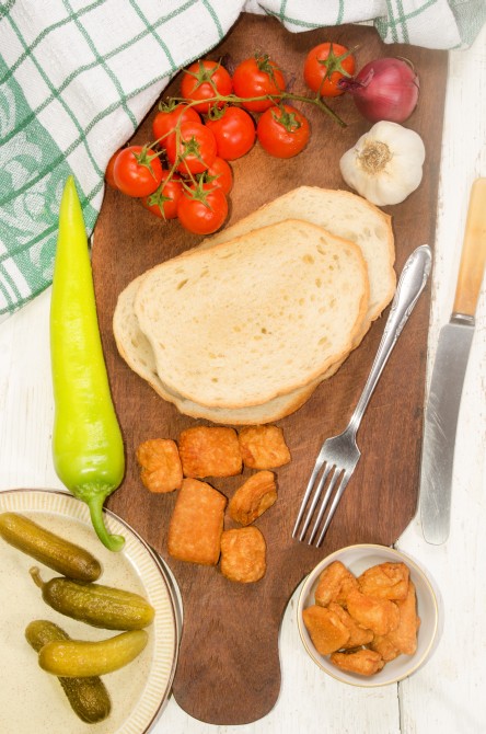 hungarian breakfast with home made bread, crackling, cherry tomato, onion, garlic, gherkin, fork and knife on wooden board hungarian breakfast with home made bread, crackling, cherry tomato, onion, garlic, gherkin, fork and knife on wooden board