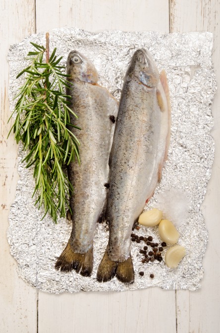 trout on aluminum foil with rosemary, salt, pepper corn and garlic