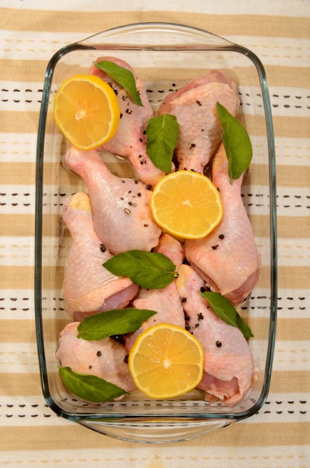 raw chicken drumstick with sage and lemon slice in a glass bowl