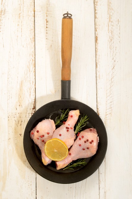 raw chicken drumstick with red peppercorn, lemon slice and rosemary in a pan on white rustic table