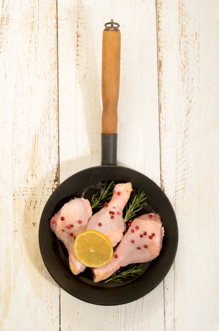 raw chicken drumstick with red peppercorn, lemon slice and rosemary in a pan on white rustic table raw chicken drumstick with red peppercorn, lemon slice and rosemary in a pan on white rustic table