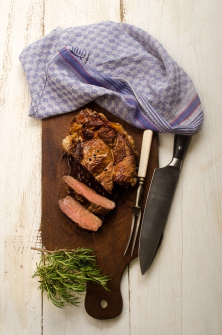 roasted beef shoulder with meat fork and knife and rosemary on wooden board