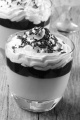 dessert with butterscotch, red fruit jelly, whipped cream and chocolate sprinkle in a glass on rustic wood