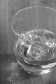golden scottish whisky in a glass with ice cube and reflection on brown wood