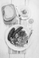 hungarian meal with fried potato, kolbasz, tomato and paprika, slice bread on wooden board, glass with palinka and plate with cucumber salad 